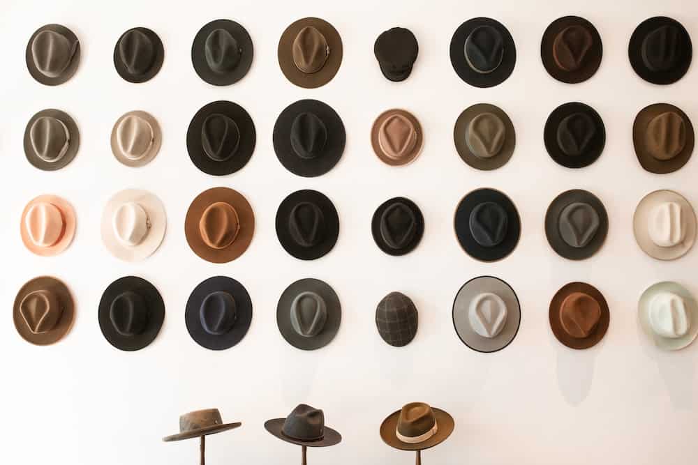 A row of hats on a wall with three hats on hat stand