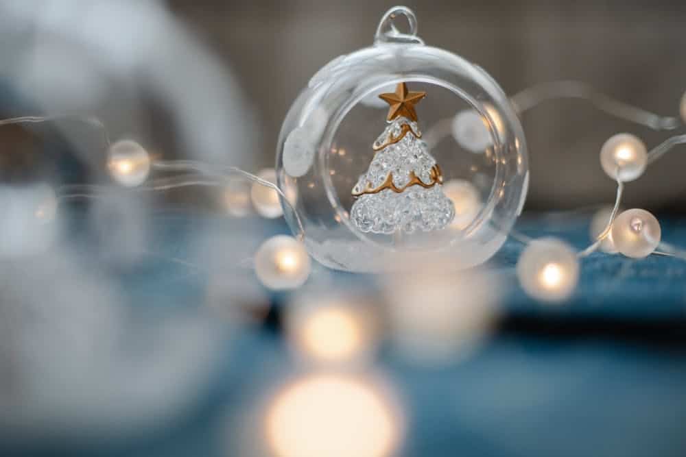 Glass ornament with a christmas tree and white lights on a blue background.
