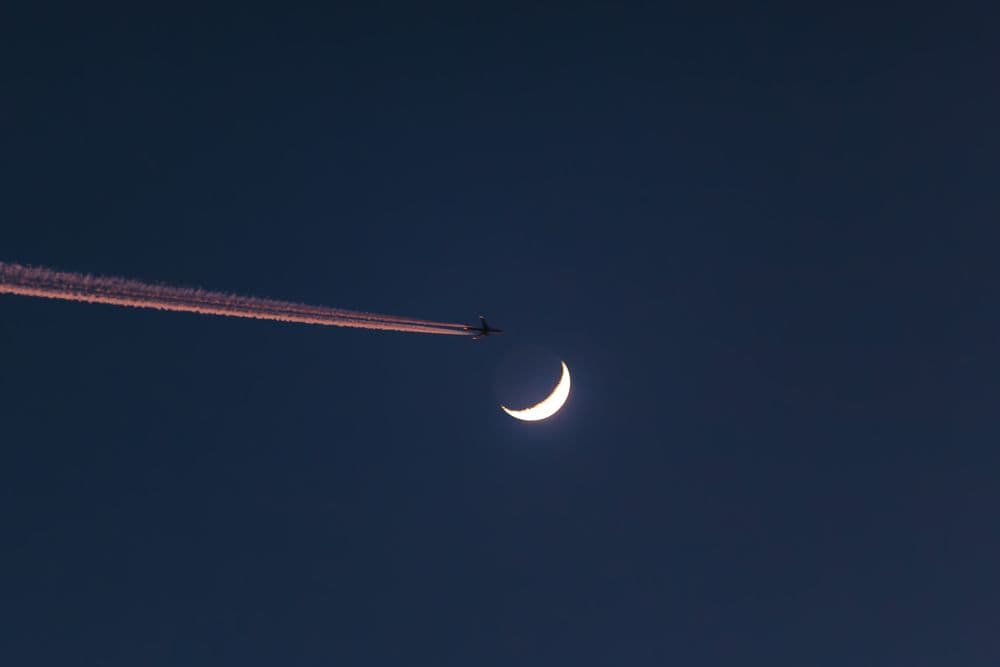 Airplane flying at night with a crescent moon